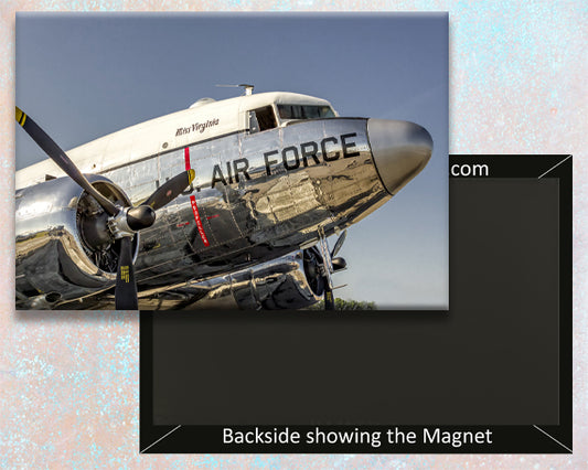 A fridge magnet of a DC-3 Air Force military aircraft with a clear mylar covering over it, set against a backdrop sky.